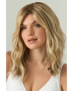 Woman in a just past the shoulders light ash brown wavy wig with long side-swept bangs and dark roots