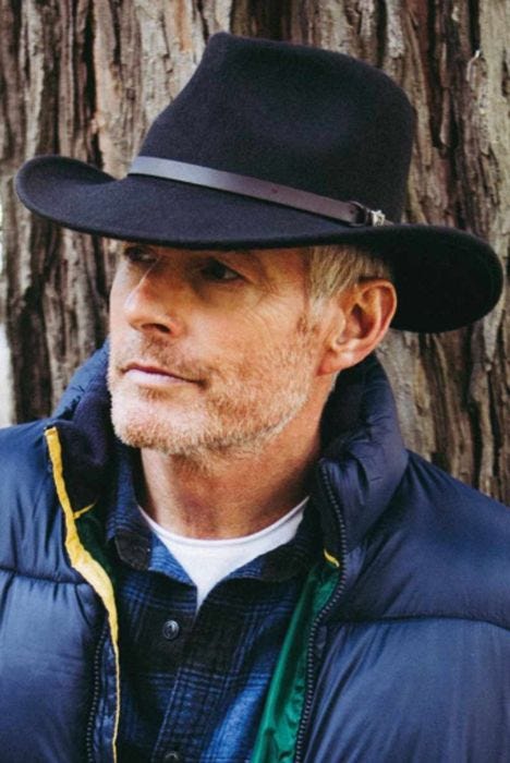 Older man outdoors in black brimmed Australian outback hat with brown leather band