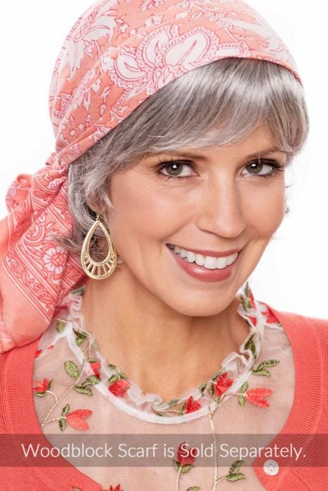 Woman in a short wavy grey halo wig with bangs under a head scarf