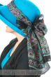 Woman in teal hat with long rectangular scarf tied around the hat for decoration