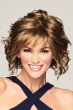 Woman in a past the chin length dark blonde layered curly wig with fringe bangs