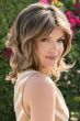 Woman in a past the shoulder curly medium brown wig with side bangs