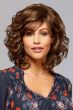 Woman in a medium brown curly wig with ample volume and side swept bangs
