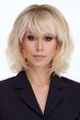 Woman in a shoulder length light blonde curly lace front wig with fringe bangs