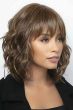 Woman in a shoulder length light brown wavy wig with shaggy bangs