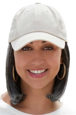 Woman in a solid beige baseball cap with shoulder length curled under light ash blonde hair attached