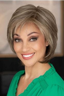 Woman in a shoulder length short light brown wig with long layers and side bangs