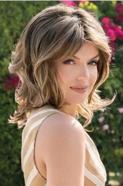 Woman in a past the shoulder curly medium brown wig with side bangs