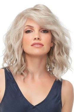 Woman in a past the shoulders light ash blonde wig with defined curls and dark roots