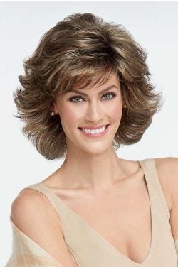 Woman in a medium brown, shoulder length blown out wig with dramatic layers and fringe bangs