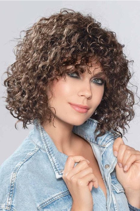 Woman in a shoulder length volume infused curly layered bob wig with curly bangs