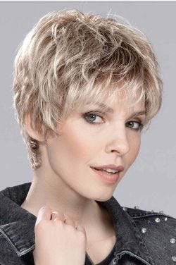 Woman in a classic light blonde pixie wig with dark roots and choppy bangs