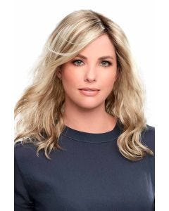 Woman in a just past the shoulders light ash brown wavy wig with long side-swept bangs and dark roots