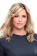 Woman in a just past the shoulders light ash brown wavy wig with long side-swept bangs and dark roots