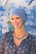 Woman outdoors by blue background wearing light denim blue colored snood hat