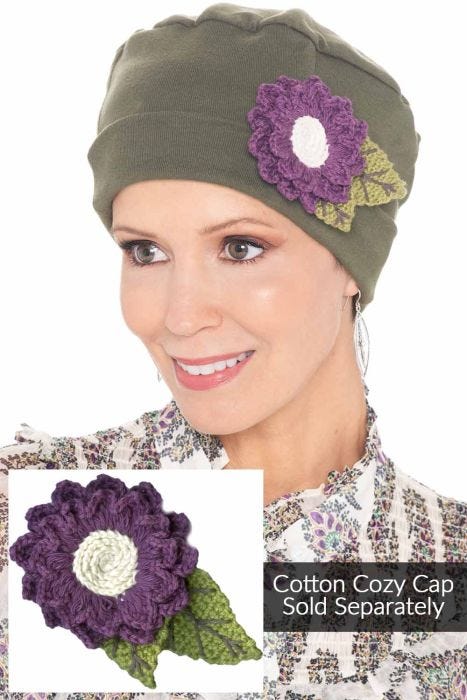 Woman in an olive cozy cap with a crocheted purple daisy pin attached