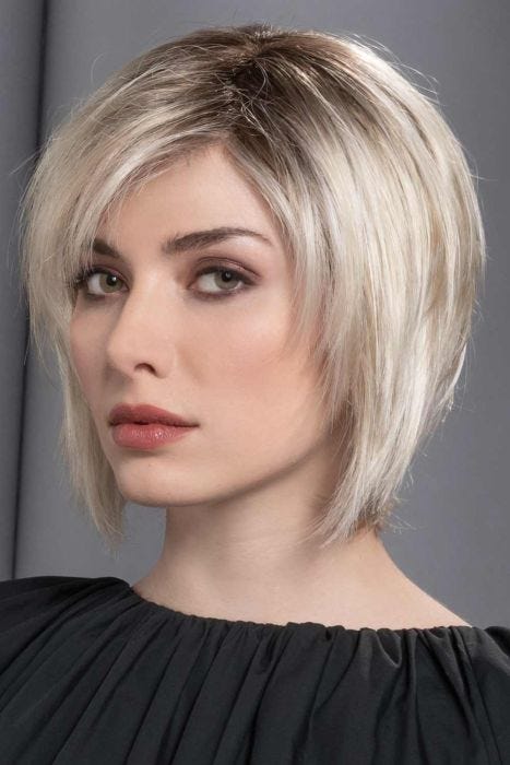 Woman in a past the chin platinum blonde stacked bob wig with choppy layers and side bangs