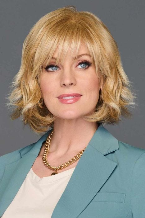 Woman in a past chin length gold blonde wavy layered wig with choppy bangs