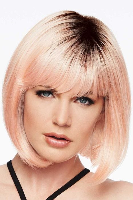 Woman in a past the chin curled under light peach bob wig with blunt bangs and dark roots