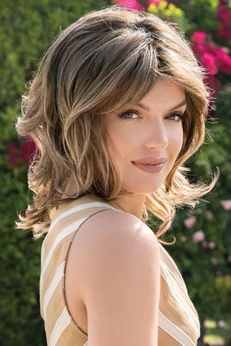 Woman in a past the shoulder curly medium brown wig with side bangs