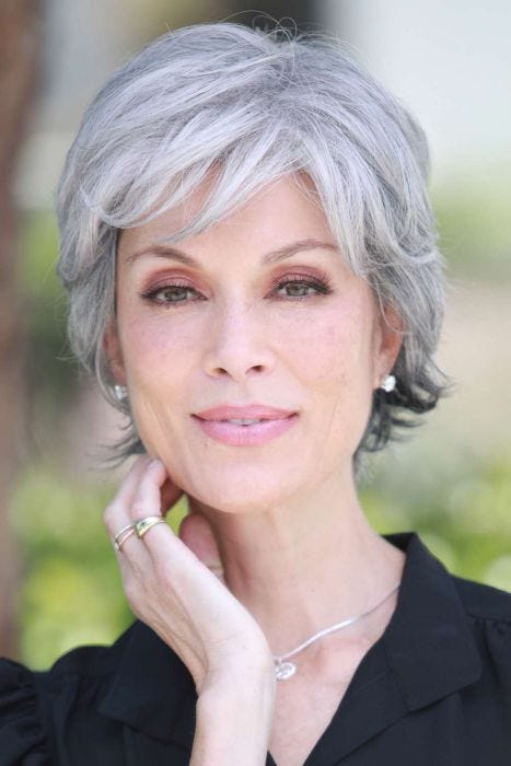 Woman in a textured light blonde pixie wig with long straight layers on top and curly short layers along the back and sides
